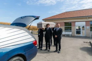 Porteurs à l'épaule devant le corbillard bleu.
